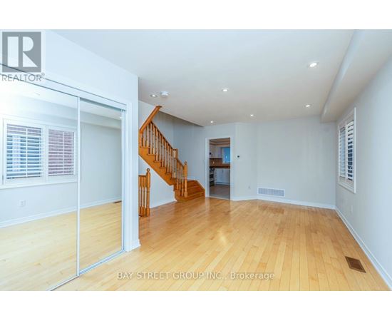 A spacious room with wooden floors and a staircase leading to another room.
