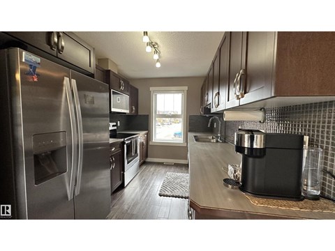 A kitchen with a stainless steel refrigerator and a black trash can.