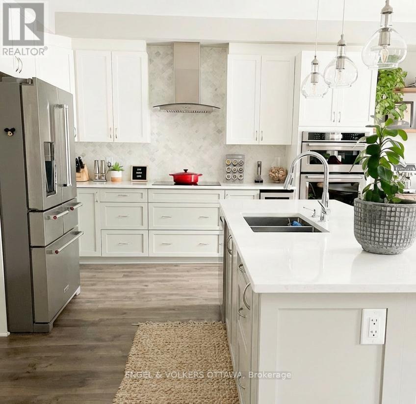A white kitchen with a refrigerator on the left and a sink with a basket of plants on the counter.
