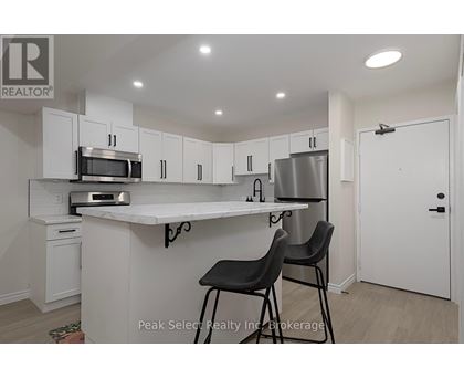 A kitchen with white cabinets and a countertop with two black chairs.