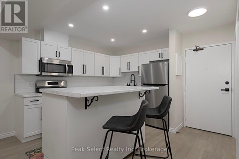 A kitchen with white cabinets and a countertop with two black chairs.
