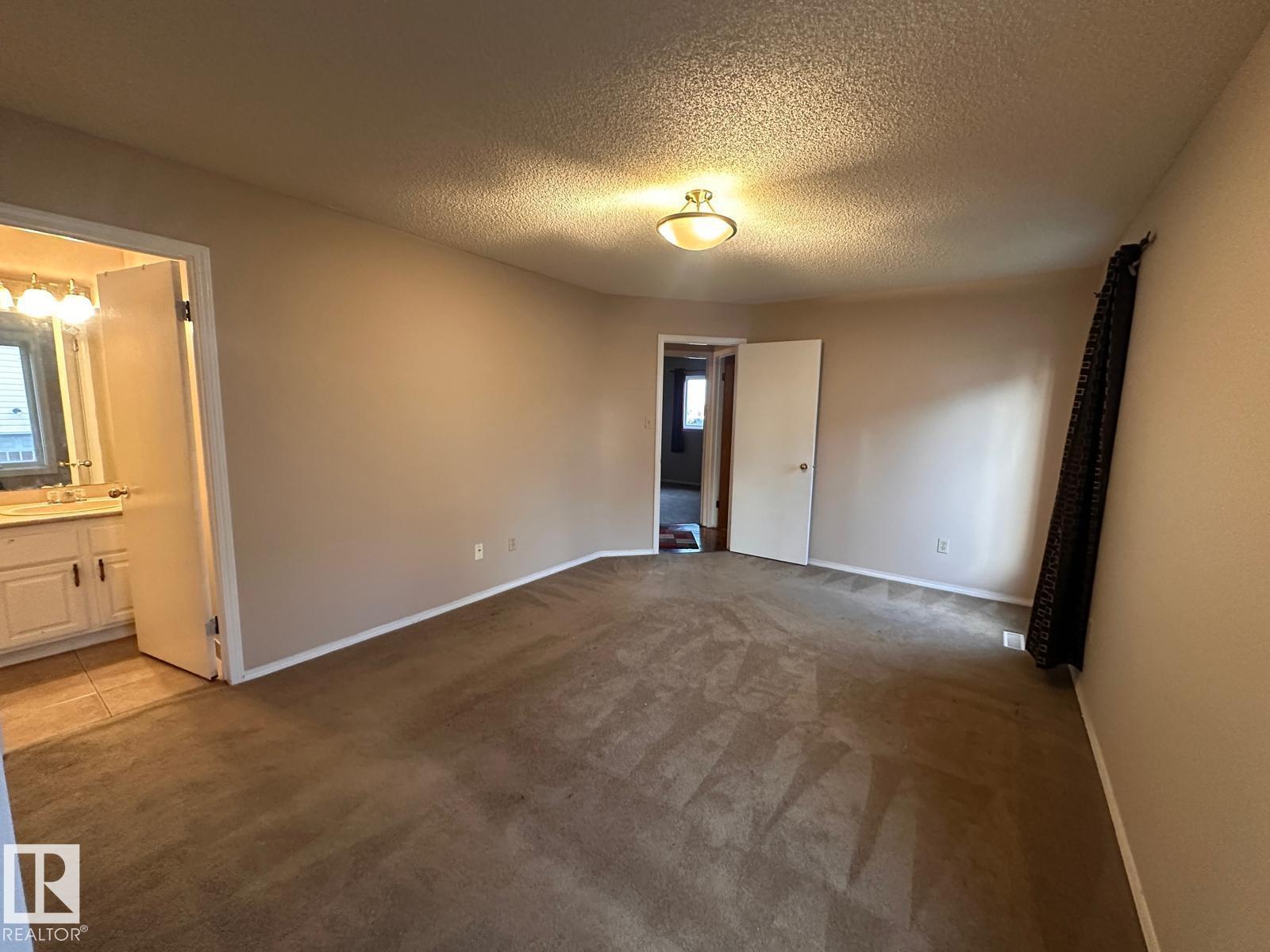 A spacious empty room with a carpeted floor and a ceiling light.