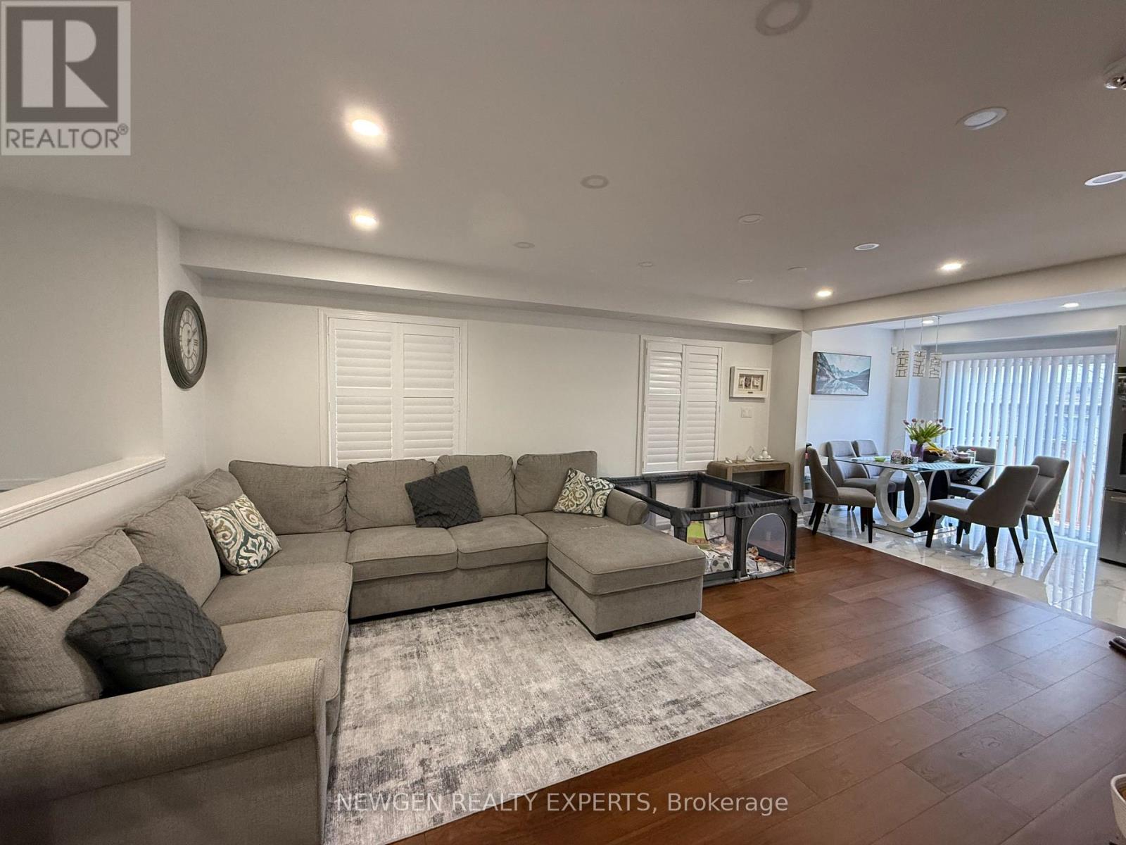 A spacious living room with a grey sofa set and a dining table with chairs.