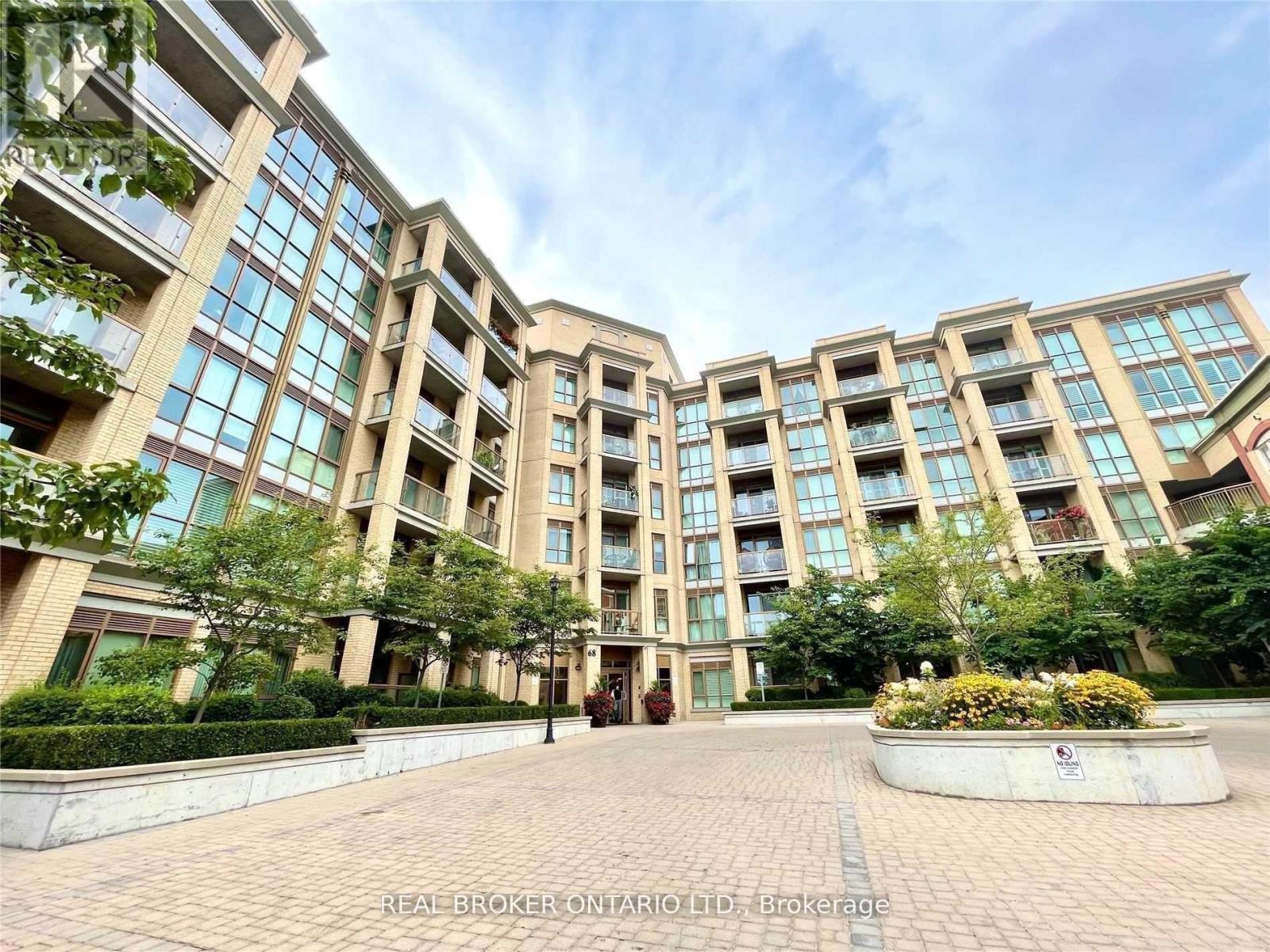 A large, modern building with many windows and balconies, surrounded by greenery and a brick walkway.