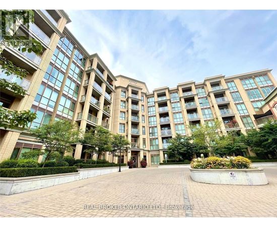 A large, modern building with many windows and balconies, surrounded by greenery and a brick walkway.