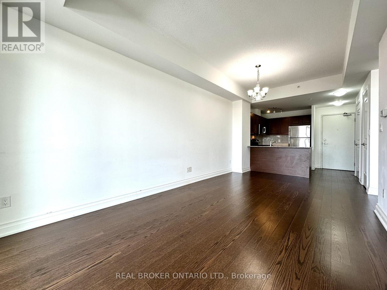A spacious room with wooden floors and a kitchen area in the background.