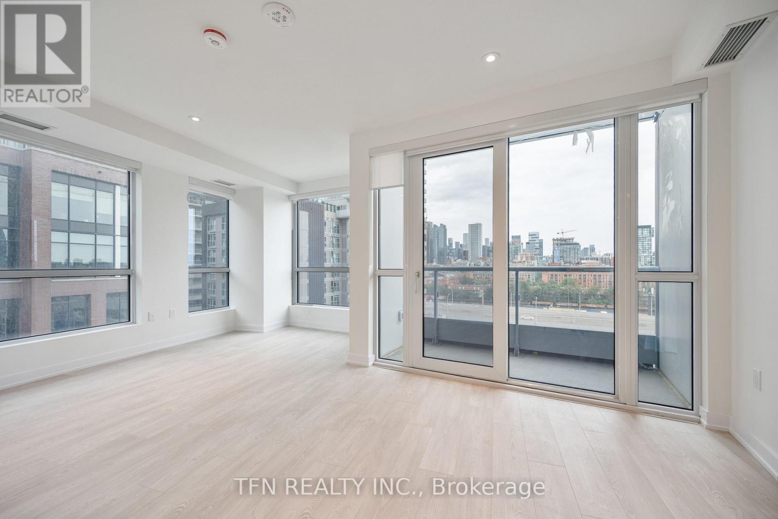 A spacious room with wooden floors and large windows overlooking a cityscape.