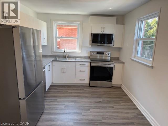 A kitchen with a refrigerator, sink, oven, and microwave.