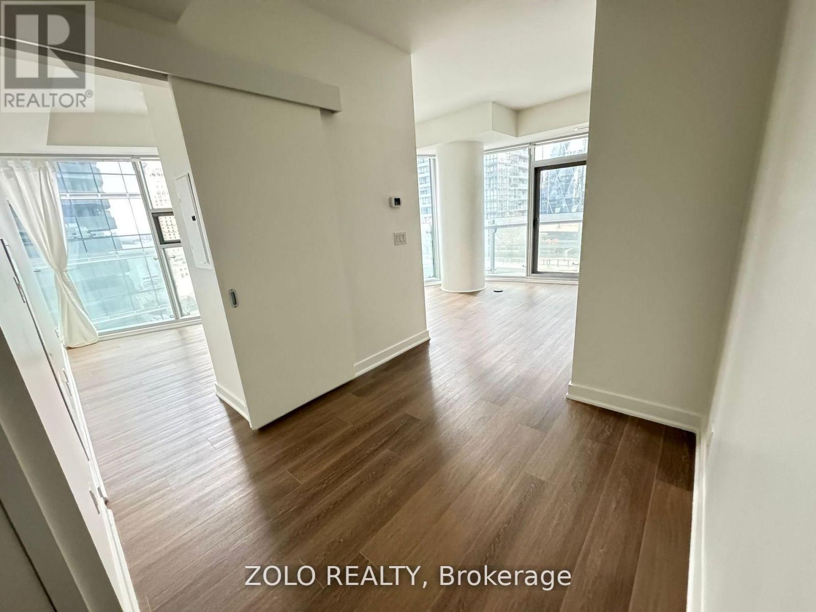 A spacious room with wooden flooring and large windows.