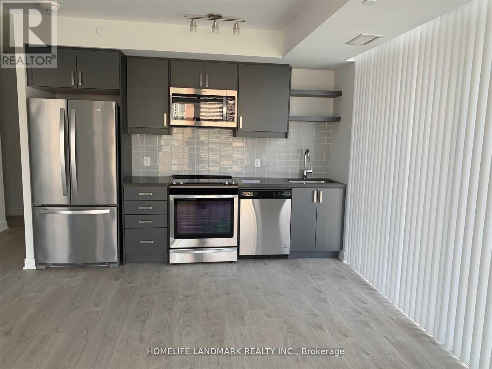 A modern kitchen with stainless steel appliances and a wooden floor.