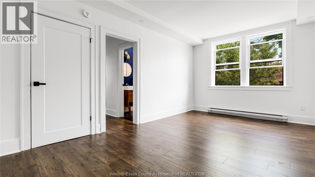 A room with a white door, a window with a view of trees, and a wooden floor.