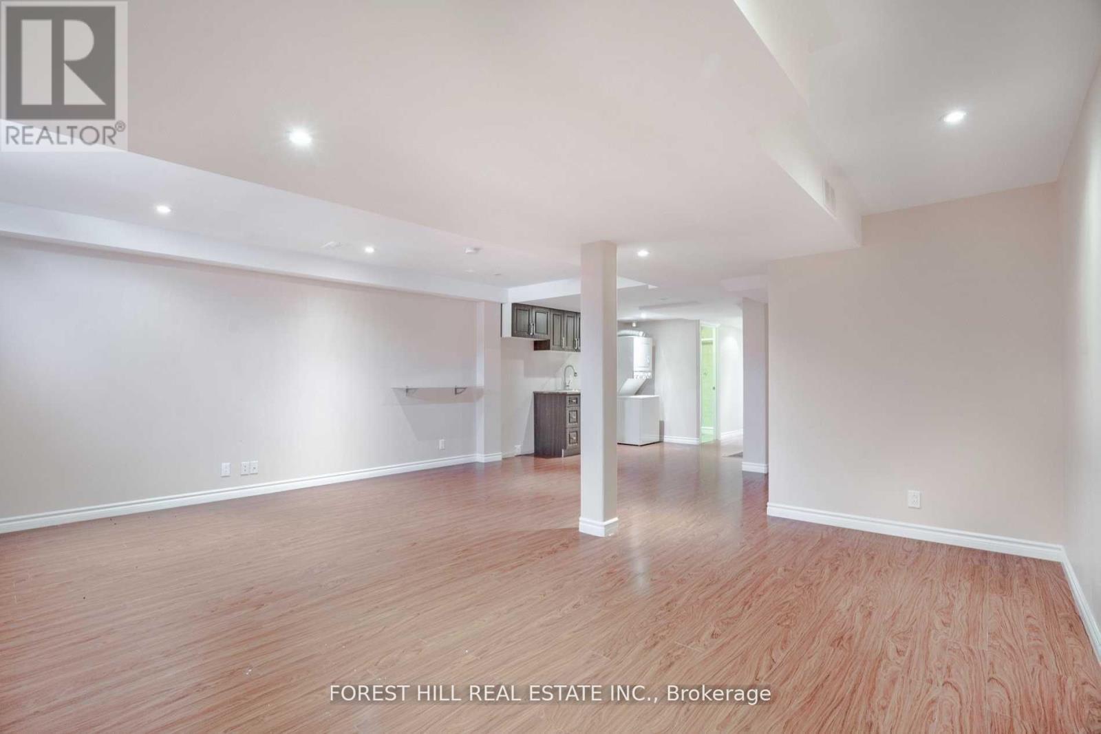 A spacious room with wooden flooring and white walls, part of a real estate listing.