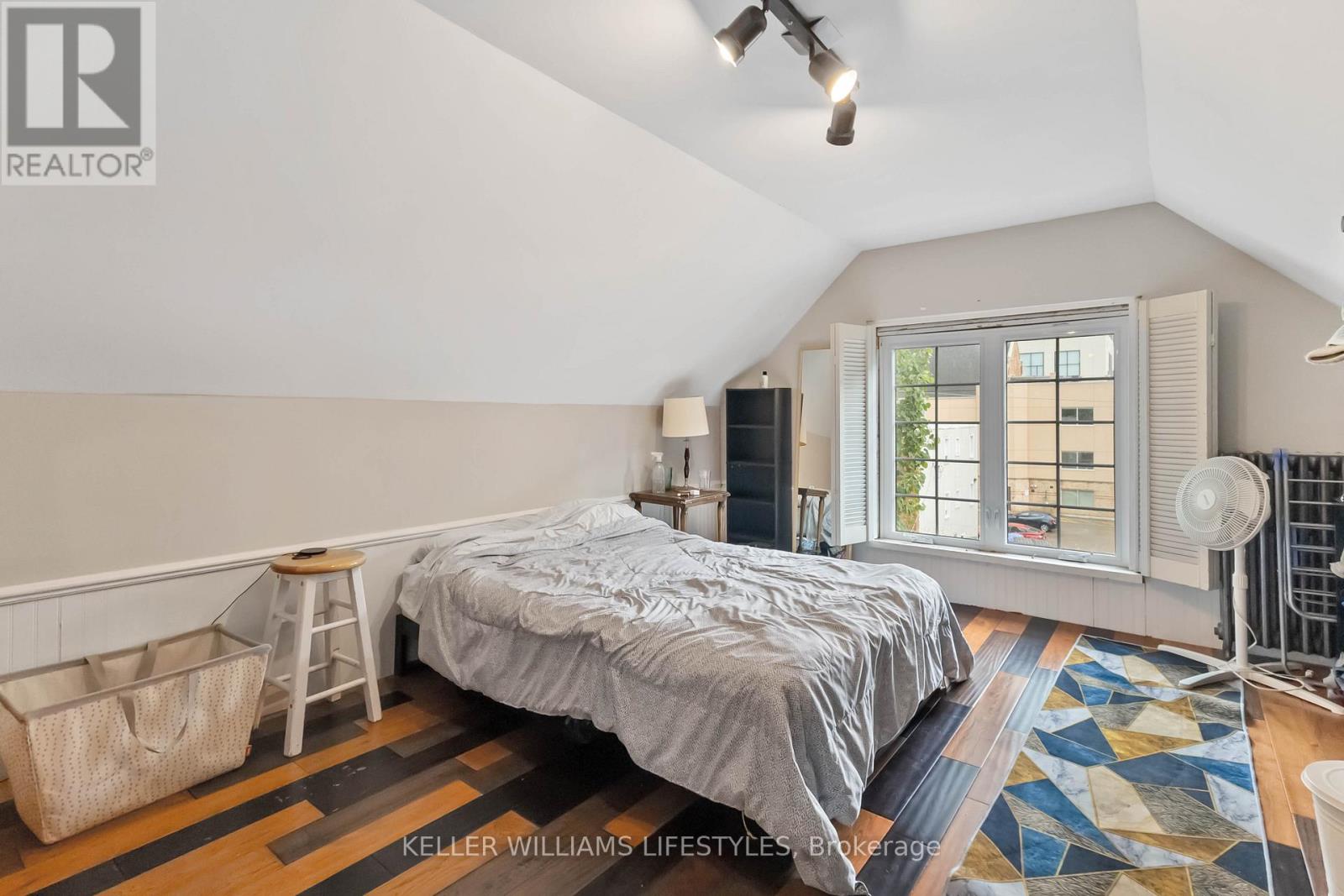 A bedroom with a bed, a window with blinds, and a rug on the floor.