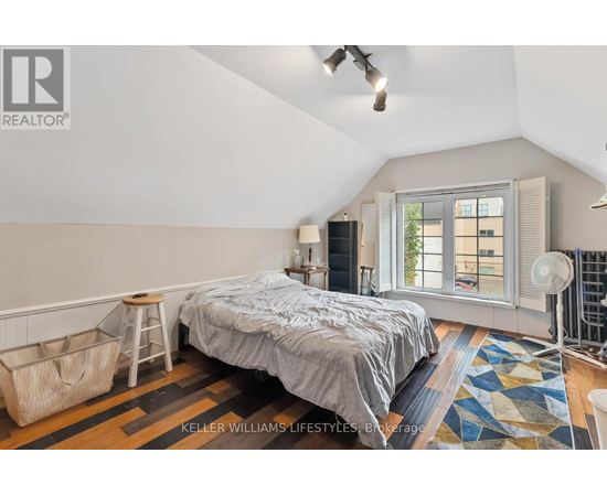 A bedroom with a bed, a window with blinds, and a rug on the floor.