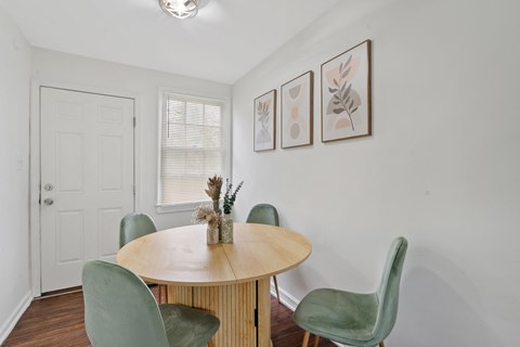 A dining room with a round table and green chairs.