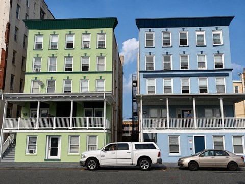 Two buildings with balconies and cars parked in front.