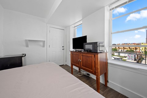 A bedroom with a bed, a television, and a window overlooking a cityscape.