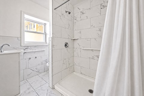 A white bathroom with a marble tile shower and a window.