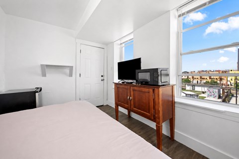 A bedroom with a bed, a television, and a window overlooking a cityscape.