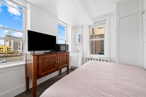 A bedroom with a large bed, a television, and a window overlooking a city street.