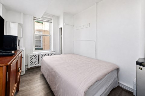 A bedroom with a bed, a television, and a window with a radiator beneath it.
