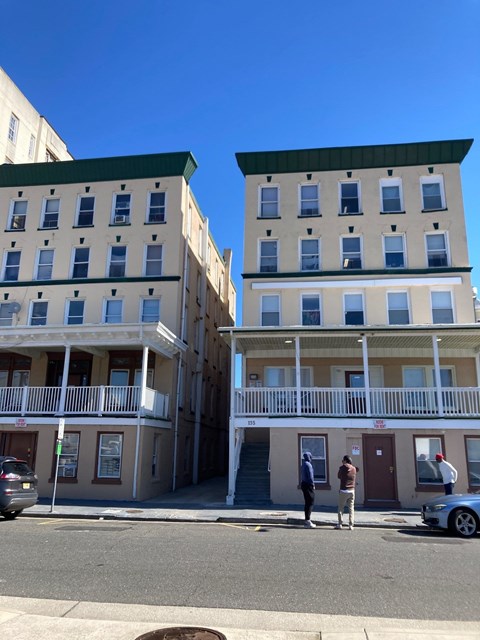 Two men are standing on the sidewalk in front of a building with a balcony.