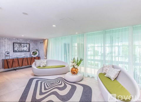A living room with a white couch, a round white table, and a rug with a black and white pattern.