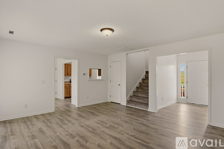 A spacious room with wooden floors and white walls, with a staircase leading to another level.