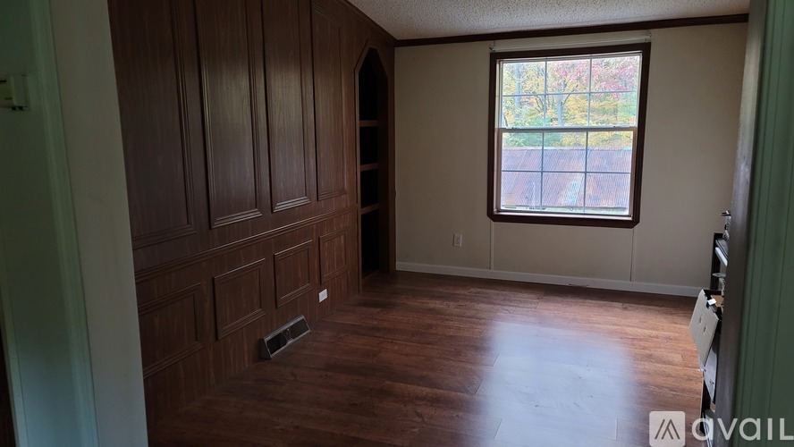 A room with wooden floors and a window with a view of trees.