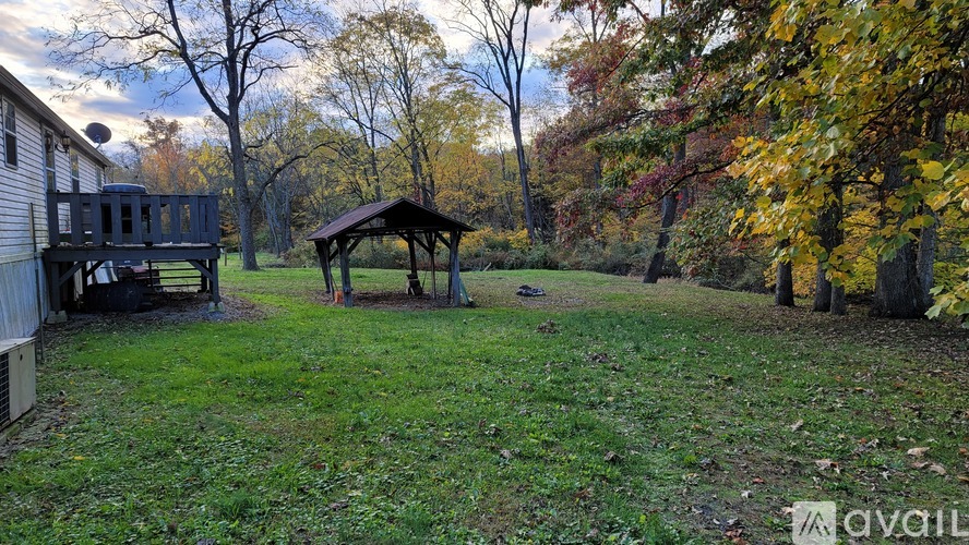 A gazebo sits in the middle of a grassy area with trees in the background.