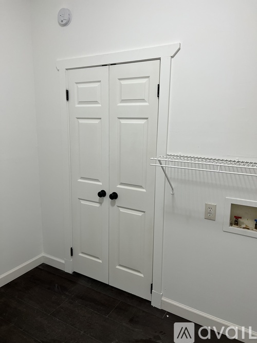 A white door with black knobs is in a white room.