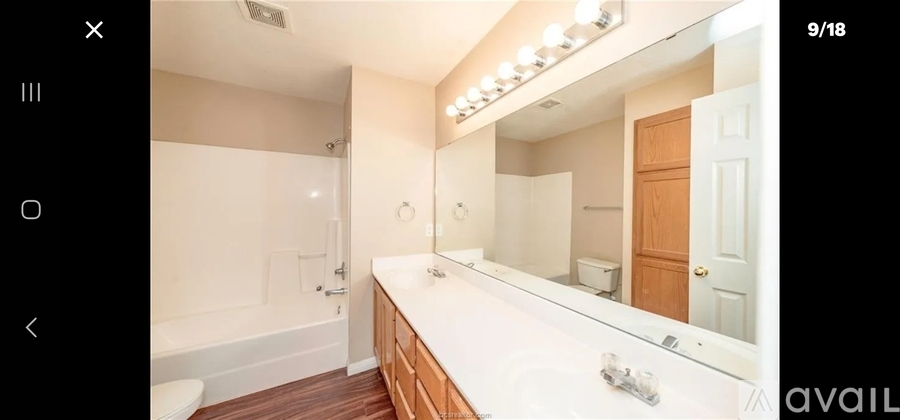 A bathroom with a large mirror and wooden flooring.