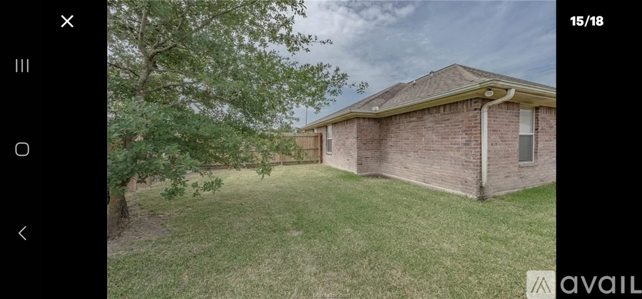 A house with a brown brick exterior and a white roof is surrounded by a grassy area and trees.