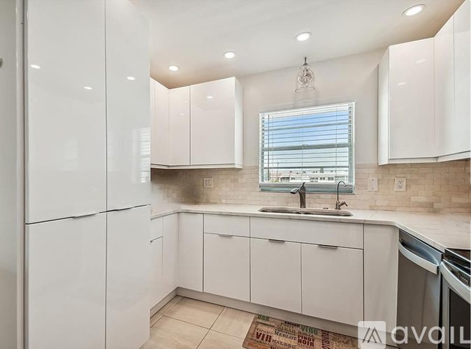 A kitchen with white cabinets and a window with blinds.
