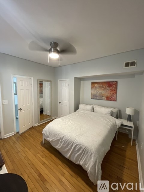 A bedroom with a bed, a ceiling fan, and a painting on the wall.