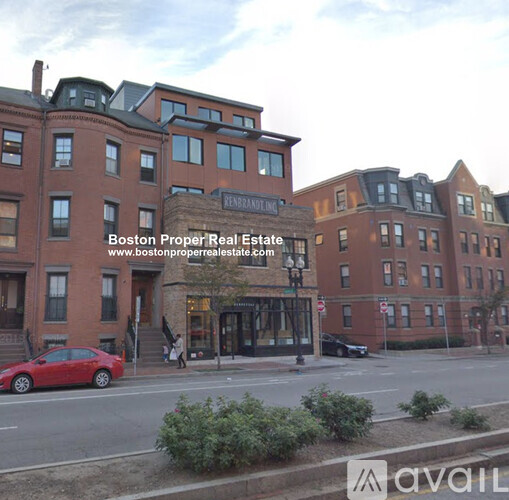 A red car is parked on the side of the street in front of a building.