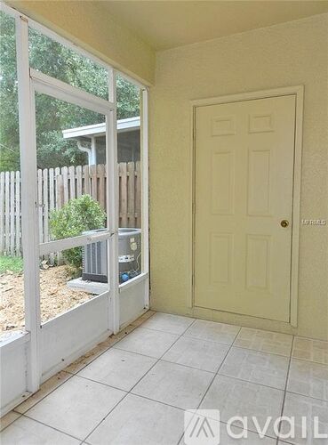 A room with a white door and a window with a view of a fence and trees.