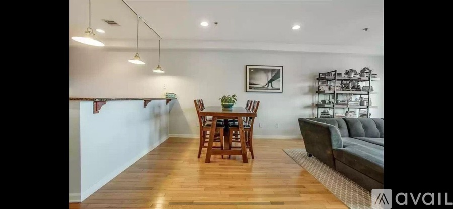 A living room with a grey couch, a wooden dining table with chairs, and a shelf with various items.