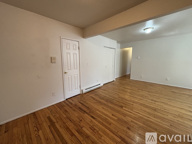 A room with wooden flooring and white walls, with a door and a window.