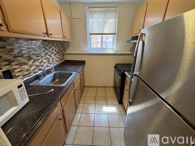 A kitchen with a stainless steel refrigerator, black countertops, and wooden cabinets.