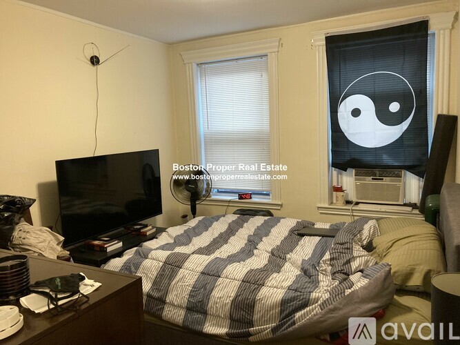 A bedroom with a bed, a television, and a window with a black and white curtain.