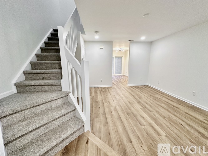 A spacious room with wooden flooring and a staircase with a carpeted runner.