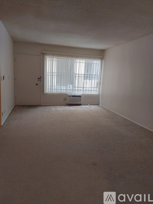 A carpeted room with a door and a window with blinds.