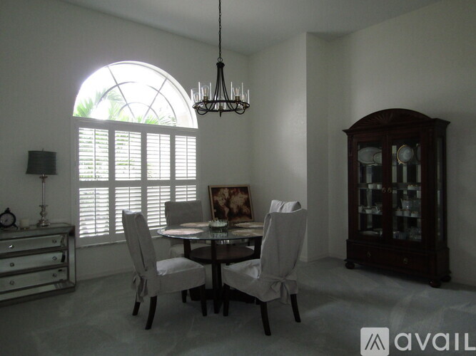 A dining room with a round table and chairs, a chandelier, and a cabinet.