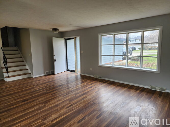 A room with wooden flooring and a large window overlooking a street.