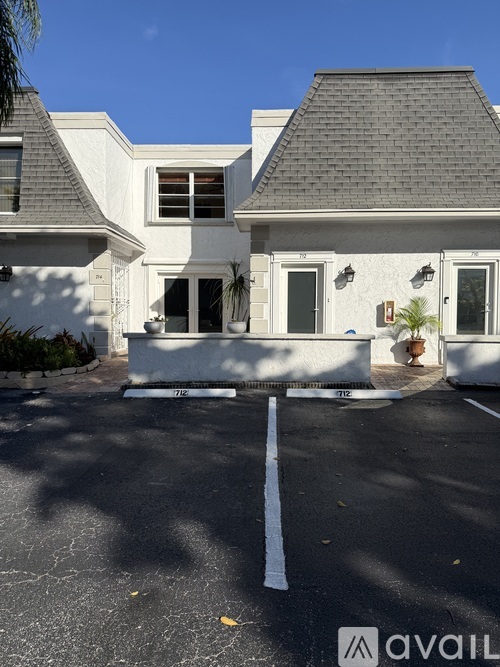 A white house with a grey roof and a sign that says "AVAIL" on the ground in front of it.