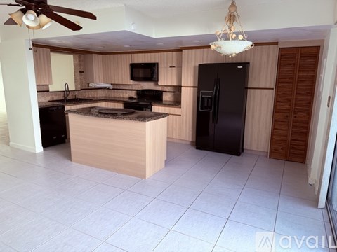 A kitchen with a black refrigerator and a ceiling fan.