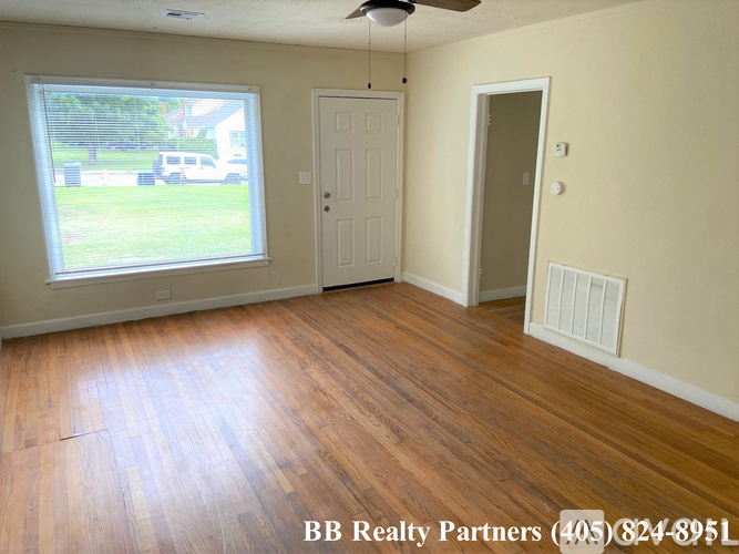 A room with wooden floors and a window showing a view of a yard and a vehicle.