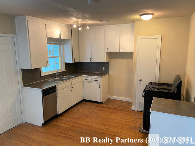 A kitchen with white cabinets and a wooden floor.