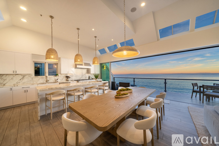 A modern kitchen with a dining table and chairs with a view of the ocean.